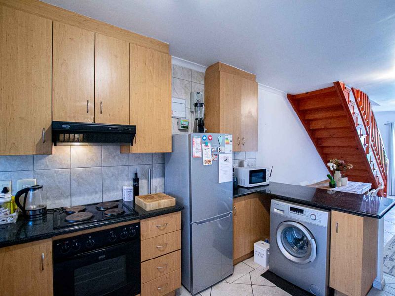 A functional kitchen featuring light wood cabinetry, granite countertops, built-in oven and hob, and tiled finishes, with an adjacent staircase leading to the upper level.