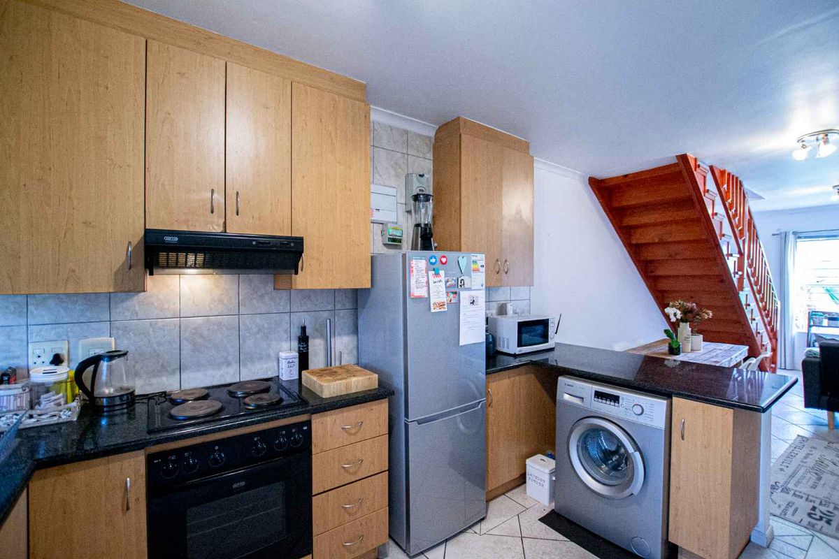A functional kitchen featuring light wood cabinetry, granite countertops, built-in oven and hob, and tiled finishes, with an adjacent staircase leading to the upper level.