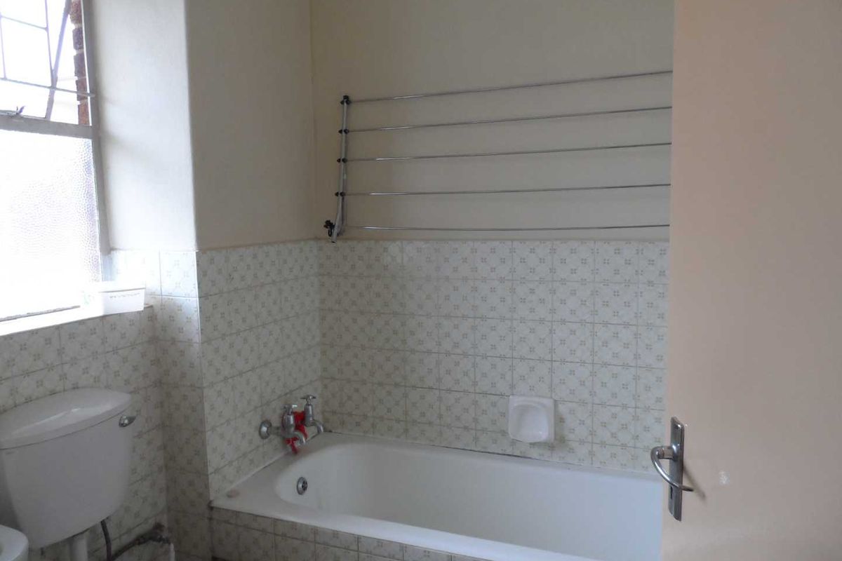 A dated bathroom featuring a standard bathtub, wall-mounted drying rack, and tiled splashbacks, requiring cosmetic updates to modernize the space.