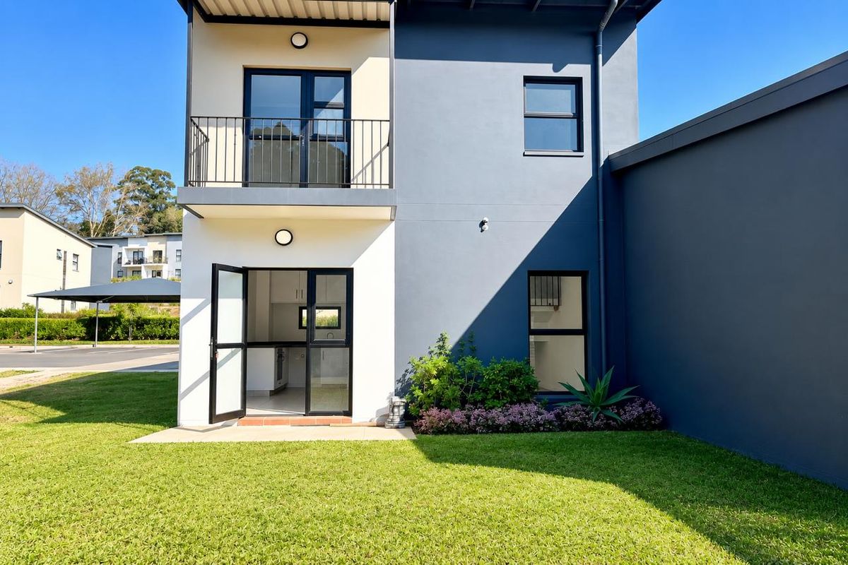 Rear view of a modern two-story townhouse featuring a private garden, a balcony with metal railing, and large glass sliding doors.
