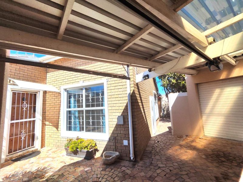 A paved rear courtyard area featuring a covered patio, brick exterior walls, security gates, and a garage entrance.
