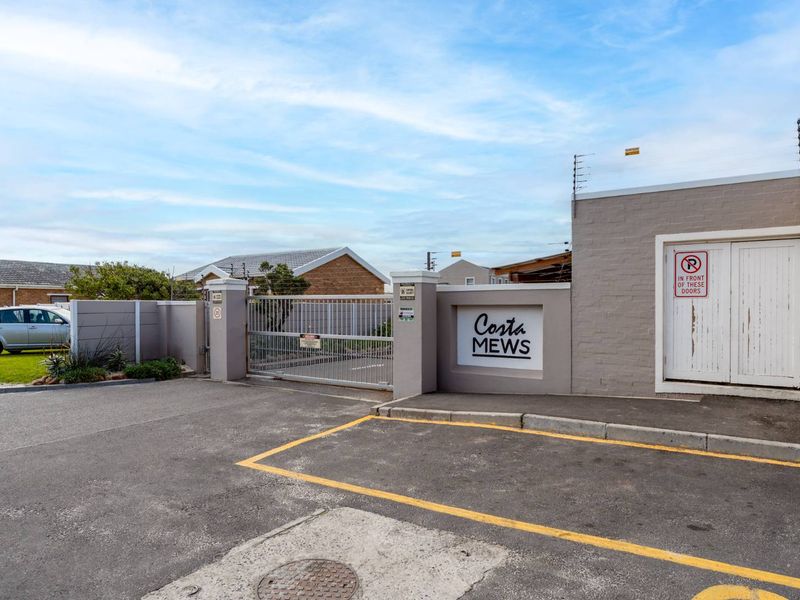 Front entrance view of Costa Mews apartment complex featuring a secure sliding gate, brick boundary wall, and electric fencing.