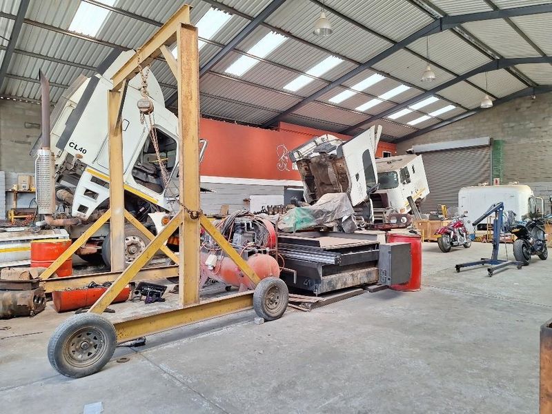 Spacious industrial workshop featuring high ceilings with skylights, concrete flooring, a gantry crane, and a large roller shutter door for vehicle access.