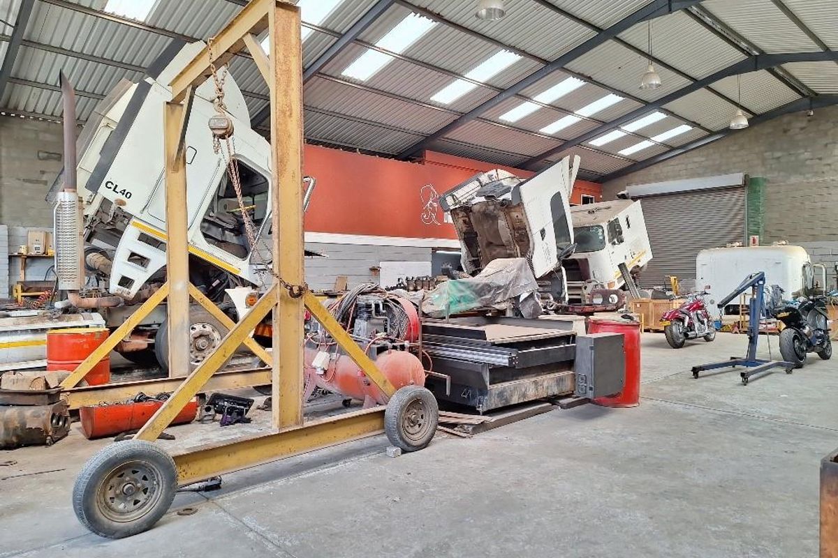 Spacious industrial workshop featuring high ceilings with skylights, concrete flooring, a gantry crane, and a large roller shutter door for vehicle access.