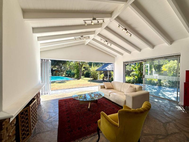 Spacious living room featuring exposed beam ceilings, stone flooring, and large bi-fold doors opening onto a garden with a swimming pool.