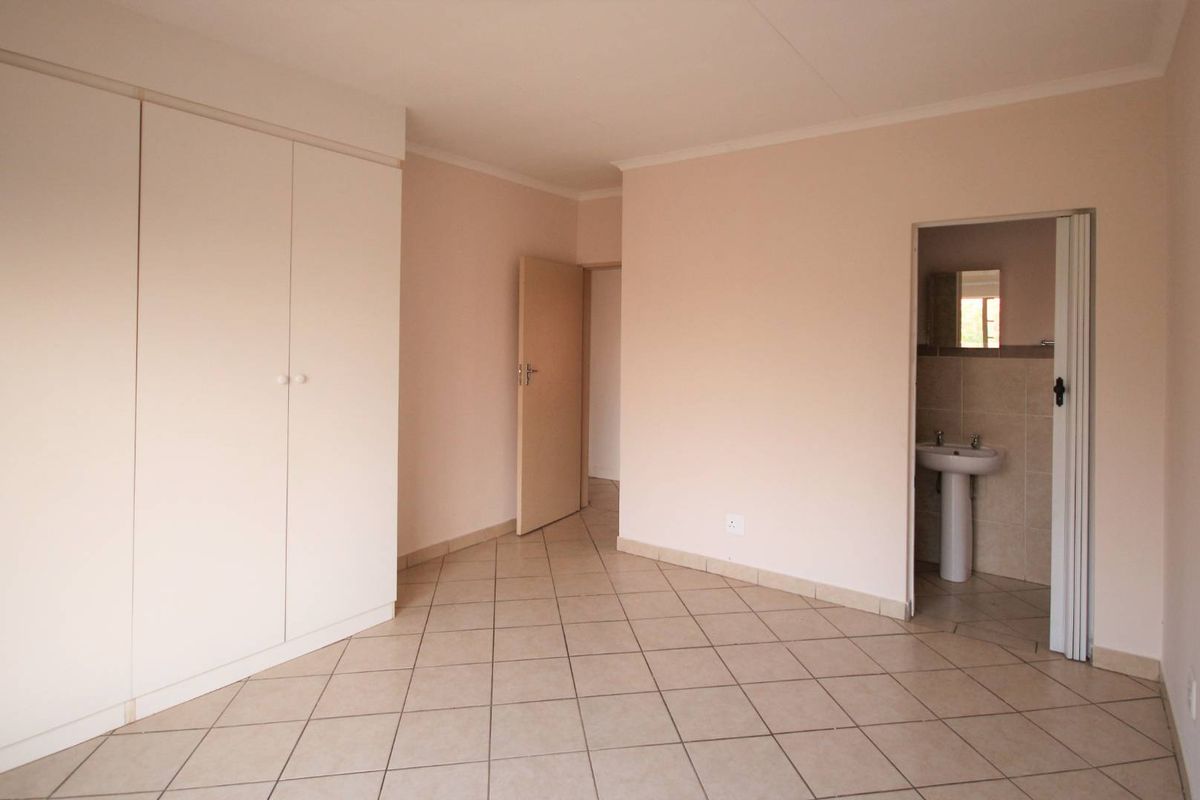 Spacious bedroom featuring neutral tiled flooring, ample built-in cupboard storage, and direct access to an en-suite bathroom with a pedestal basin.