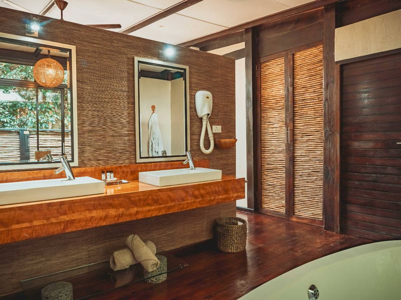 A well-appointed bathroom featuring a double vanity with vessel sinks, a rich wooden countertop, hardwood flooring, and a soaking tub with natural textured wall finishes.