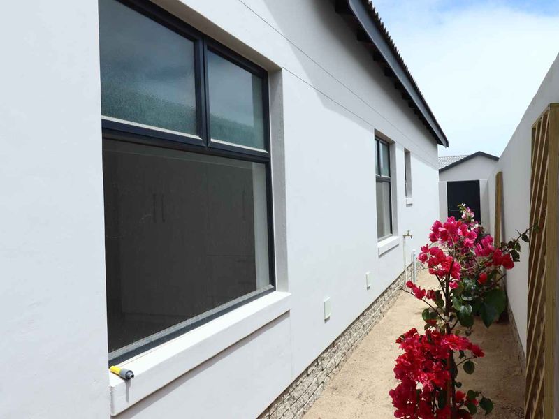 A clean side exterior view of the house featuring modern aluminium window frames, stone cladding base, and well-maintained plastered walls.