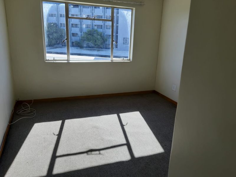 An empty bedroom featuring carpet flooring, neutral walls, and an aluminium-framed window providing natural light.
