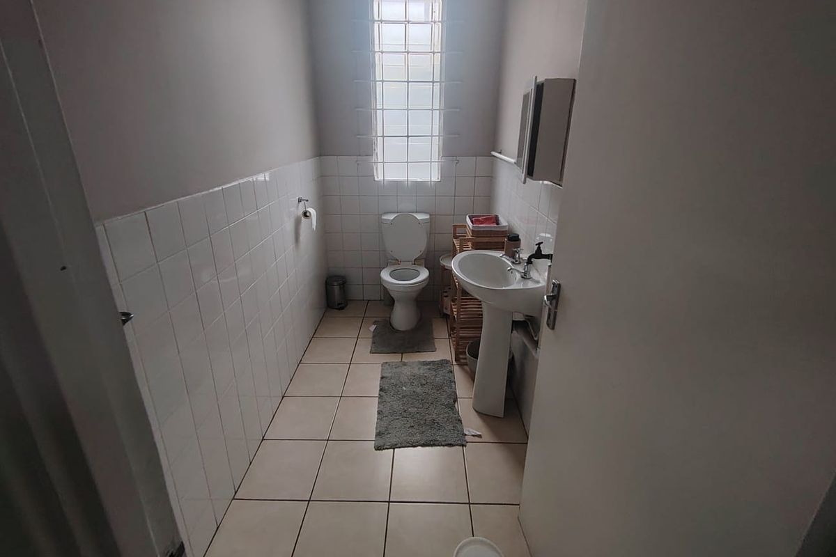 A functional bathroom featuring a pedestal basin, toilet, and glass block window, finished with white wall tiles and neutral floor tiling.