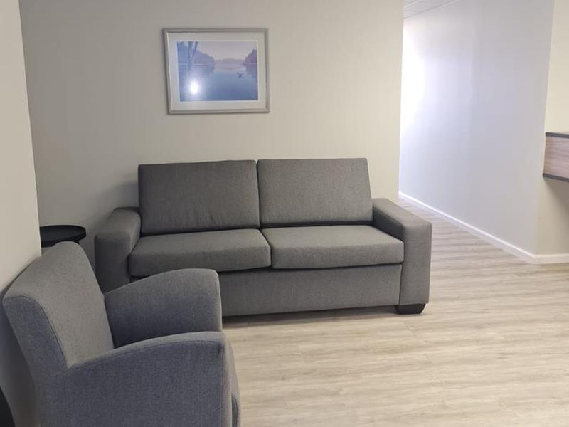 A professional office waiting area featuring neutral walls, modern laminate flooring, and a suspended ceiling with recessed lighting.