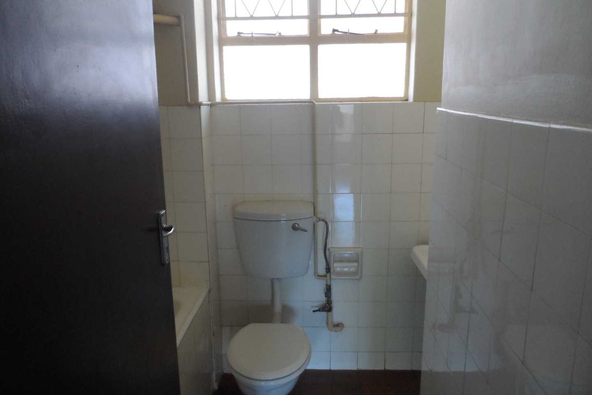 A functional bathroom featuring a toilet, bathtub, and tiled walls with exposed plumbing, requiring cosmetic updates to modernize the space.