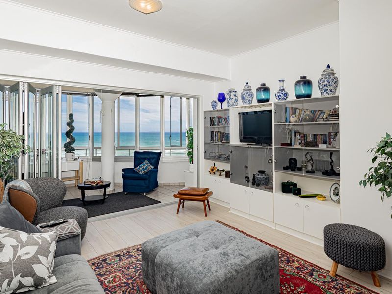 Spacious living room featuring built-in shelving, light-toned tiled flooring, and folding glass doors that open to a scenic ocean view.