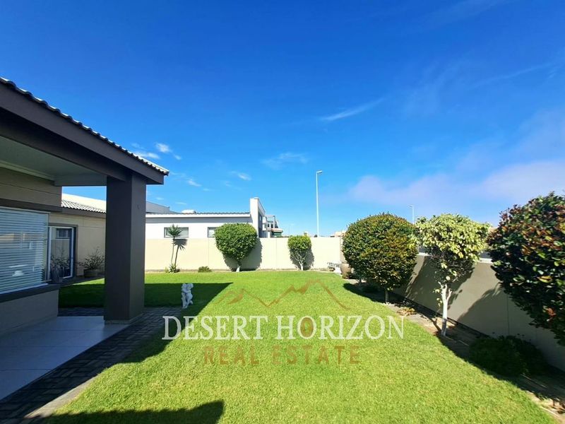 A well-maintained rear garden featuring a manicured lawn, boundary walls, and a covered patio area.