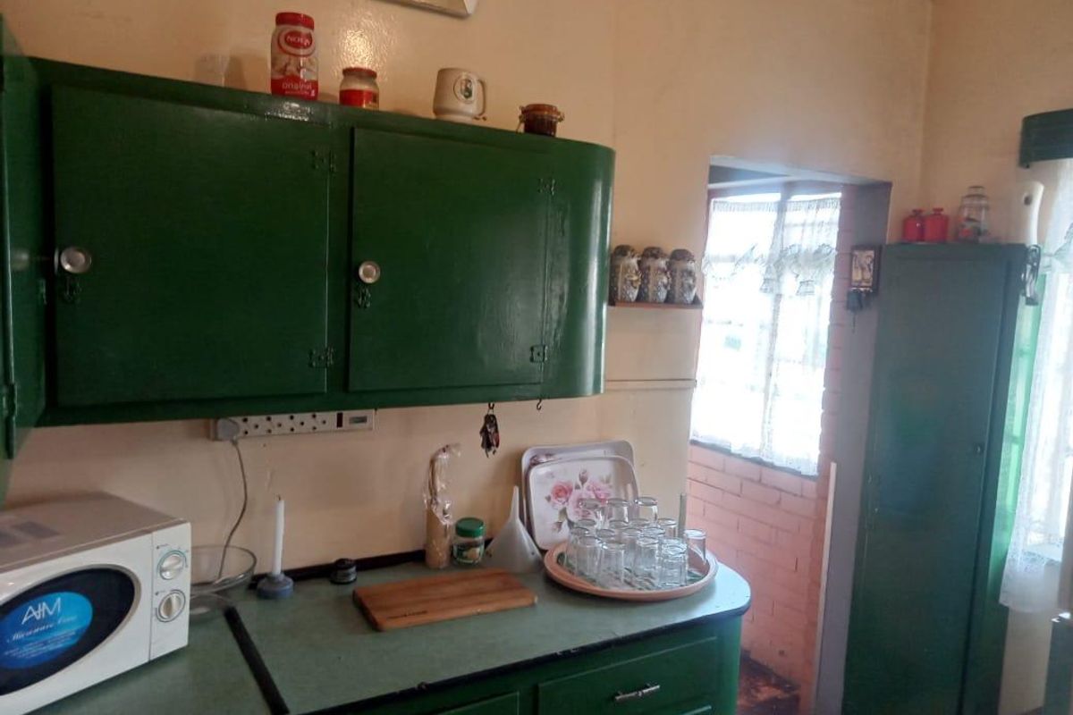 A dated kitchen featuring green painted cabinetry, laminate countertops, and direct access to an adjacent outdoor area.