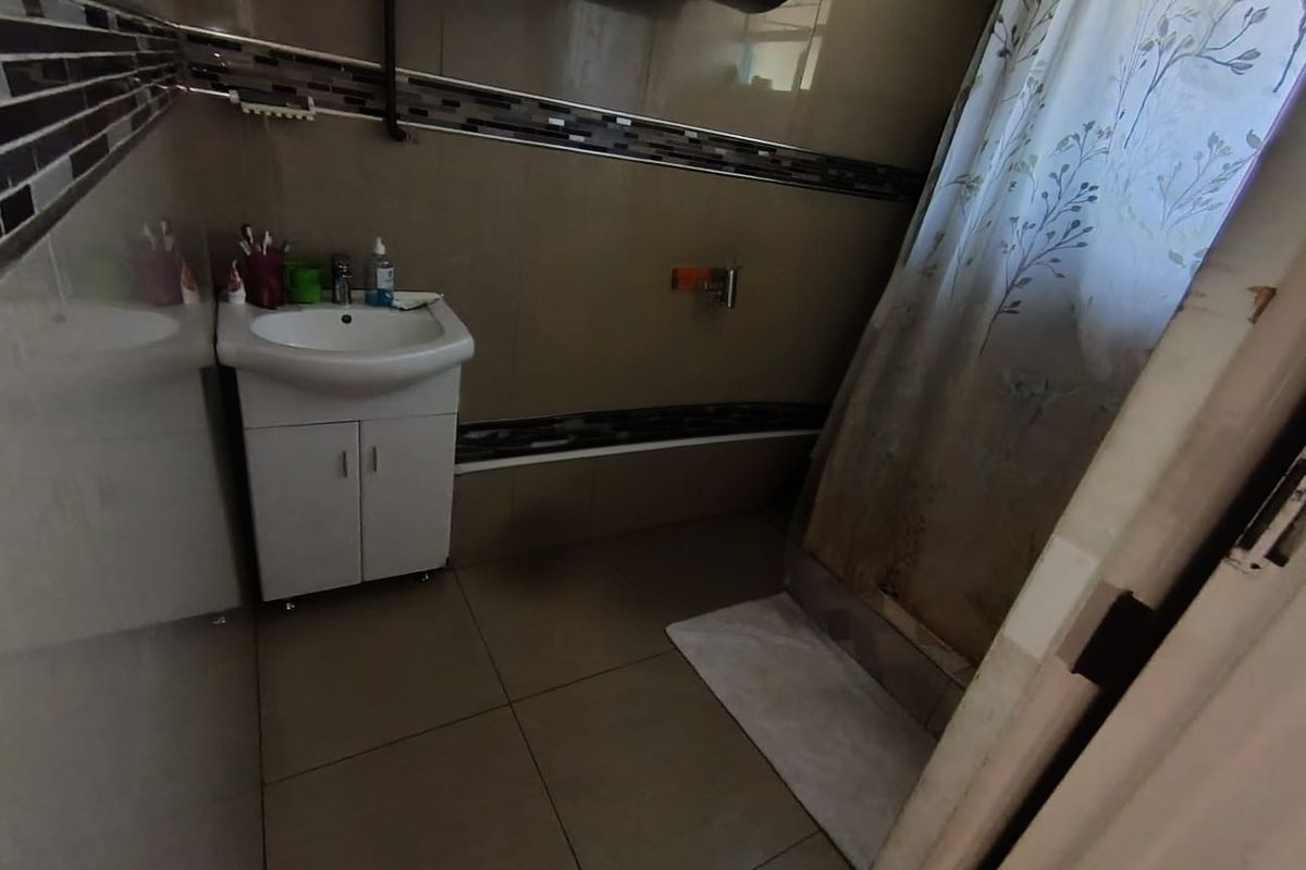 A functional bathroom featuring tiled walls and flooring, a vanity cabinet with a basin, and a shower area with a curtain.