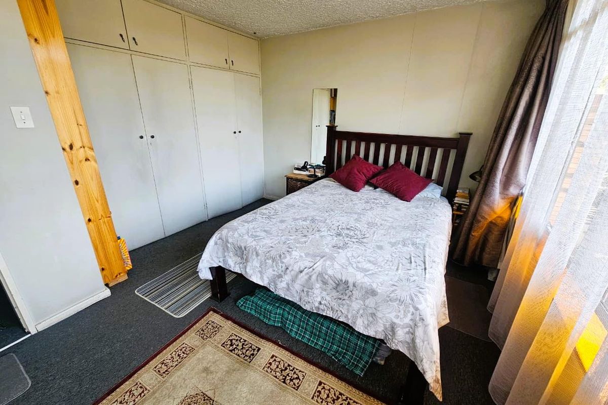 A bedroom featuring built-in storage cupboards, carpeted flooring, and a window with curtain treatments.