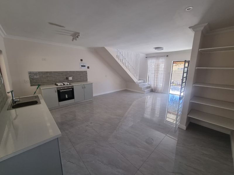 Spacious open-plan living area featuring a modern kitchen with built-in appliances, sleek floor tiles, and a staircase leading to the upper level.