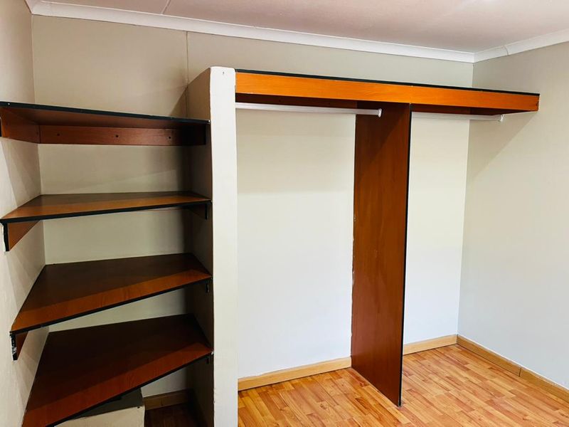 A bedroom featuring built-in wooden wardrobes and open shelving, finished with laminate flooring and neutral wall tones.