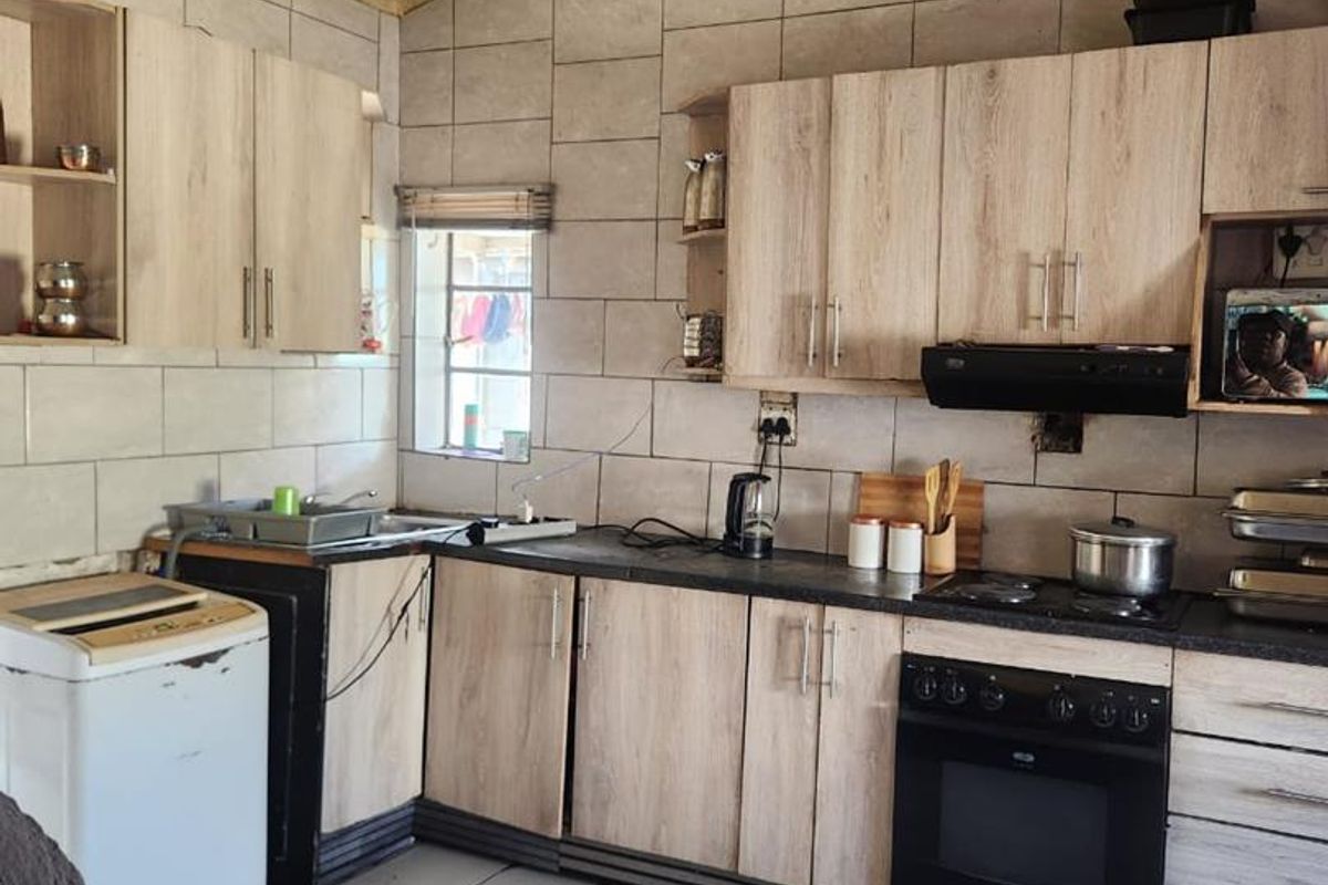 A functional kitchen featuring light wood-look cabinetry, tiled splashbacks, built-in oven, and hob, with tiled flooring throughout.
