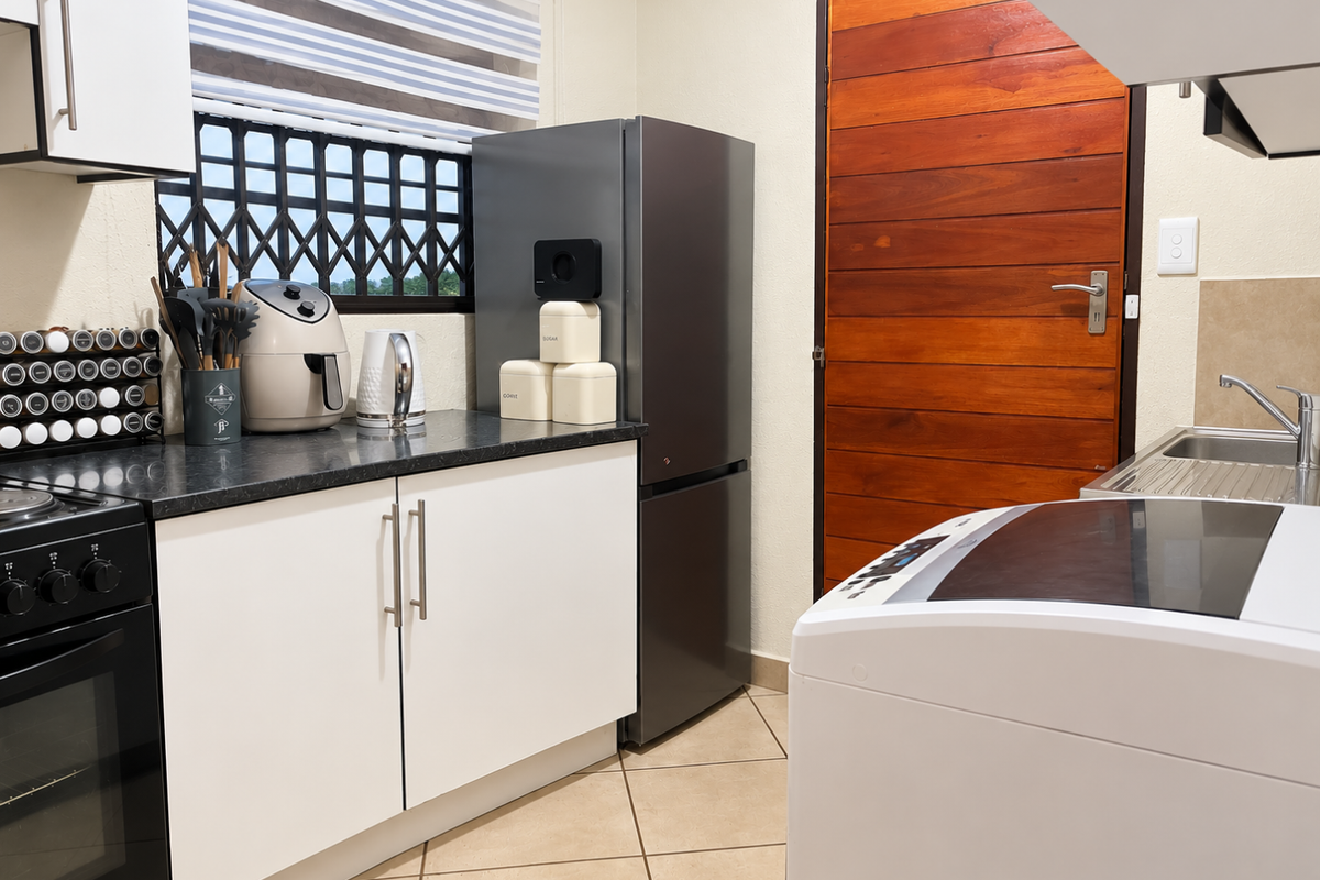 A functional kitchen featuring white cabinetry, dark laminate countertops, a built-in oven, and a stainless steel sink with tiled flooring.