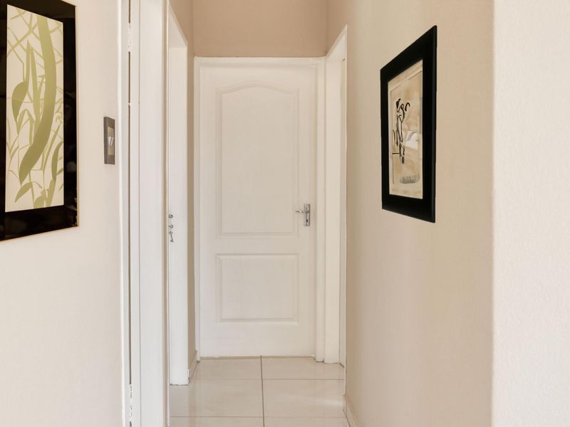A clean and well-maintained hallway featuring neutral wall tones, tiled flooring, and white internal doors.