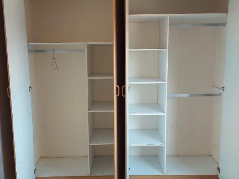 A bedroom featuring a large, multi-section built-in wardrobe with shelving and hanging rails, finished with ceramic floor tiles.