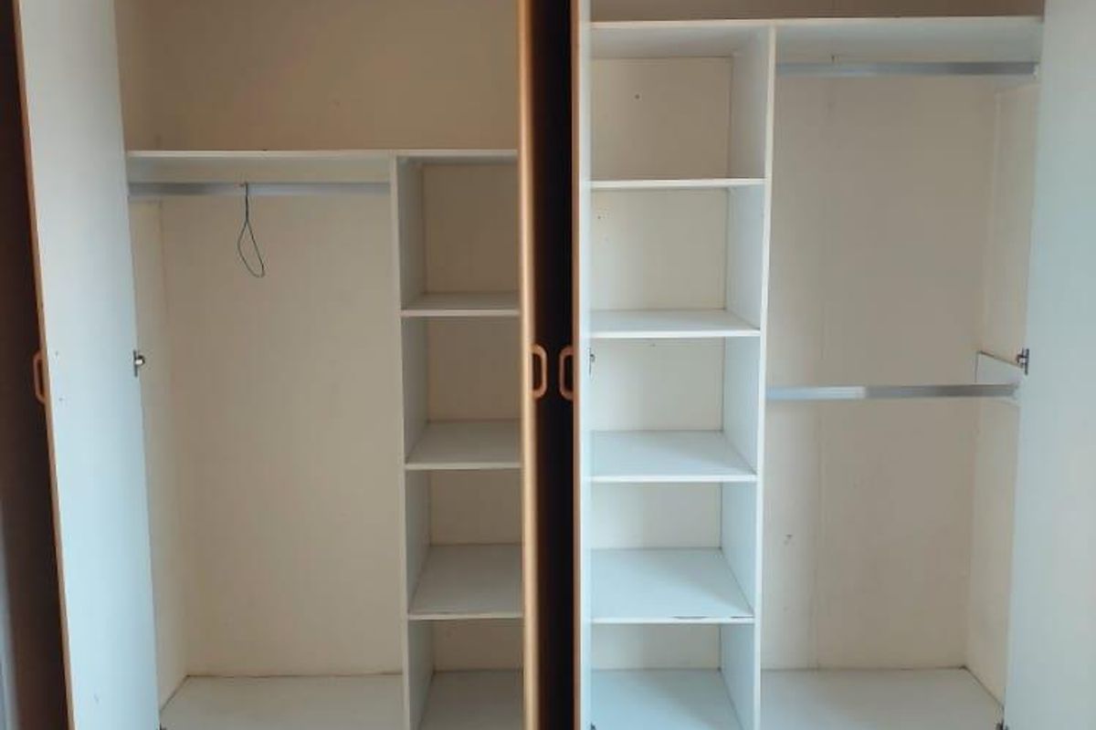 A bedroom featuring a large, multi-section built-in wardrobe with shelving and hanging rails, finished with ceramic floor tiles.