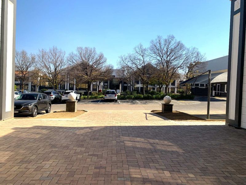 View of the office complex entrance featuring a paved driveway, stone pillar accents, and established garden landscaping.