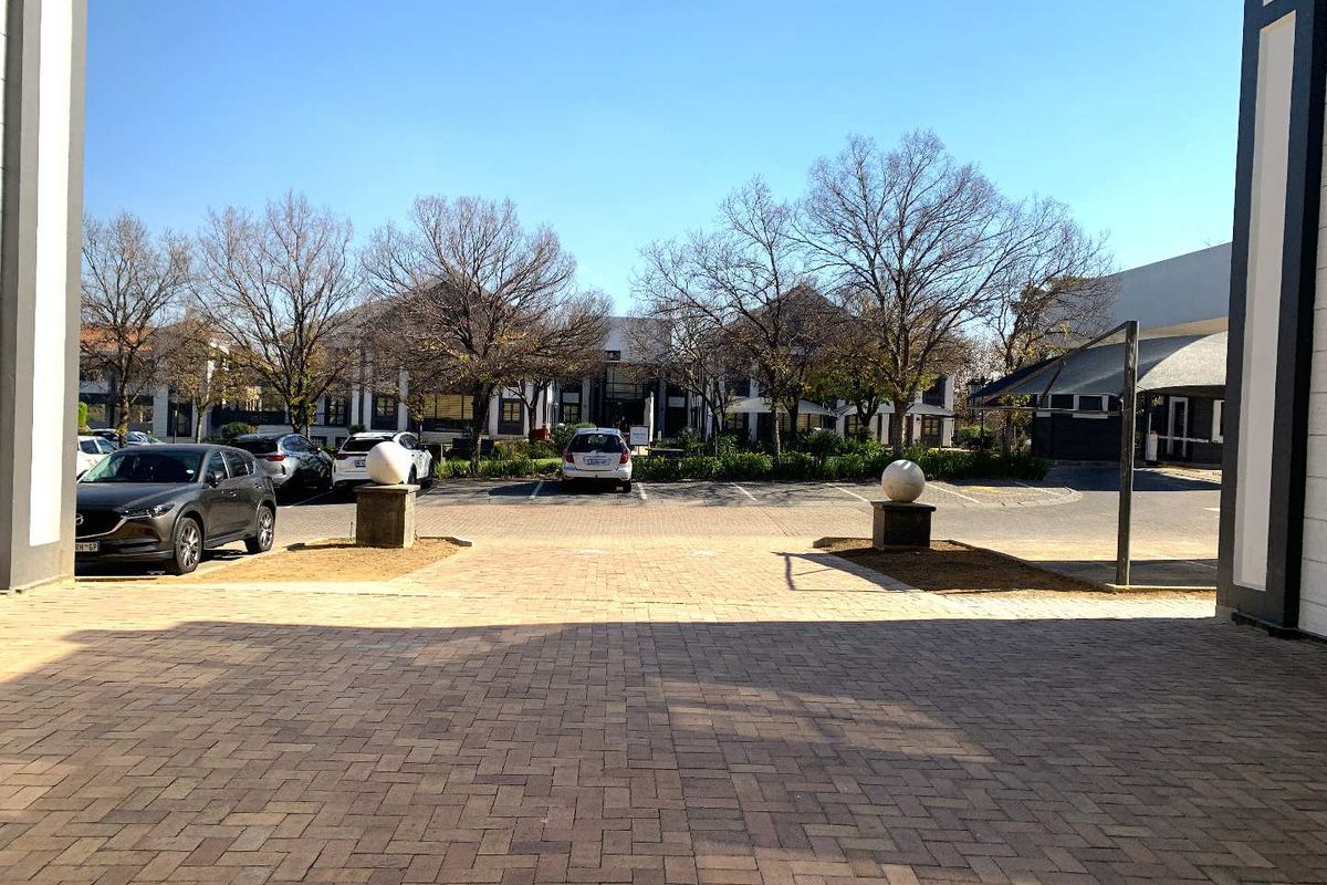 View of the office complex entrance featuring a paved driveway, stone pillar accents, and established garden landscaping.