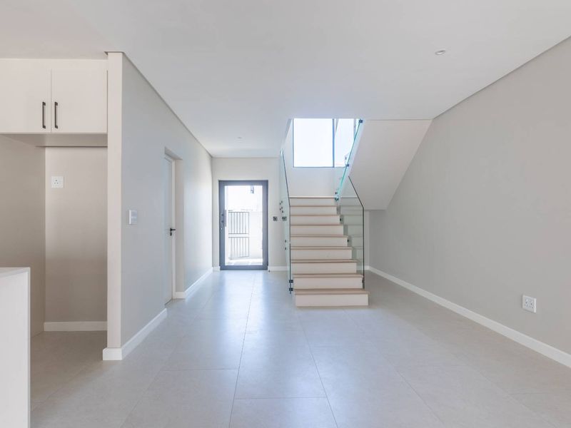 Modern open-plan living area featuring a sleek staircase with glass balustrade, neutral tiled flooring, and a contemporary kitchen with built-in cabinetry.