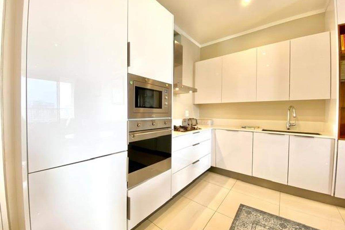 Modern kitchen featuring high-gloss white cabinetry, integrated oven, built-in microwave, stainless steel extractor fan, and sleek stone countertops.