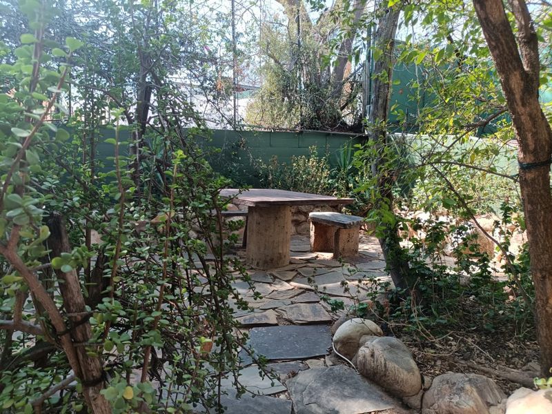 A secluded garden area featuring natural stone paving, built-in stone table and benches, surrounded by mature trees and boundary fencing.