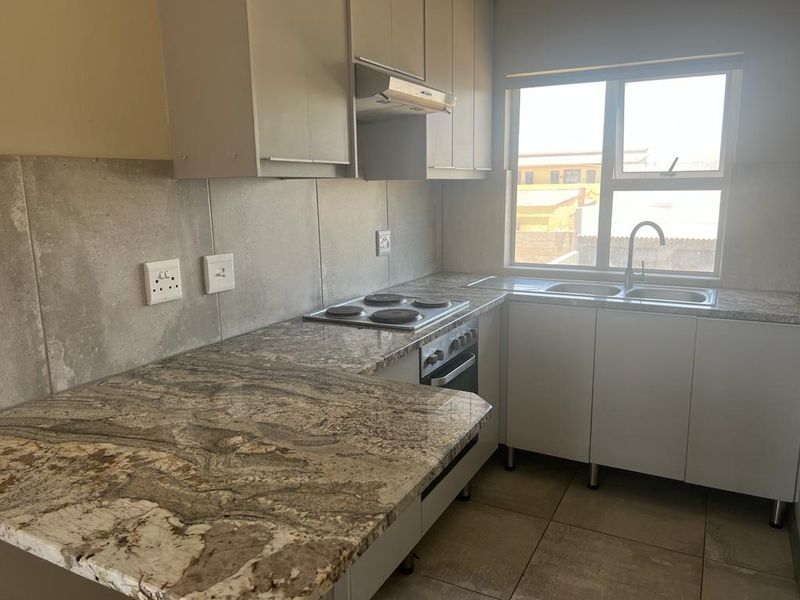 A functional kitchen featuring granite countertops, built-in oven and hob, extractor fan, and double sink with ample cabinetry and tiled finishes.
