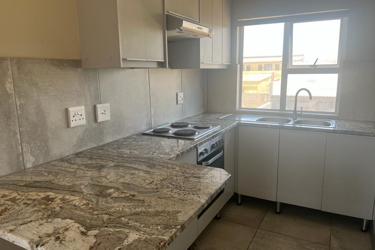 A functional kitchen featuring granite countertops, built-in oven and hob, extractor fan, and double sink with ample cabinetry and tiled finishes.