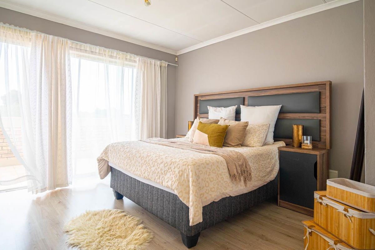 A well-lit bedroom featuring light wood-look flooring, neutral wall tones, and a sliding glass door providing access to an outdoor balcony area.