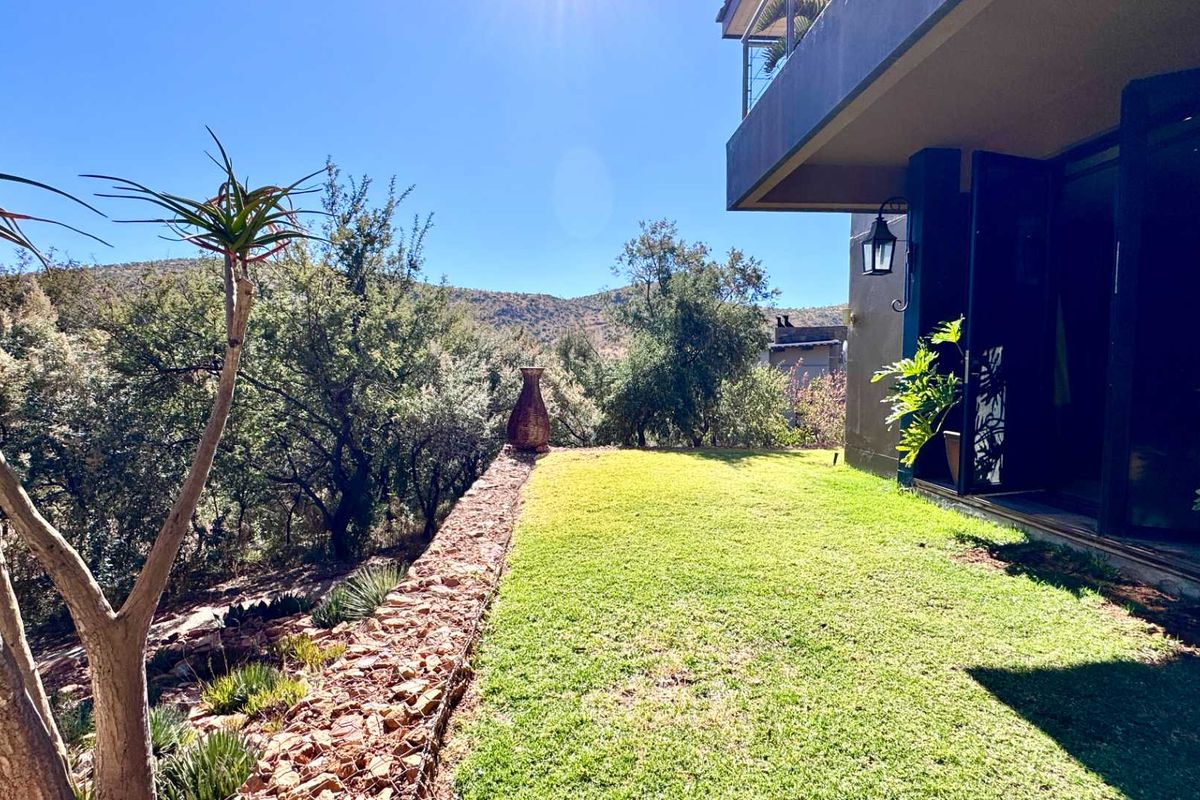 A well-maintained rear garden area featuring a manicured lawn, a stone retaining wall, and scenic views of the surrounding landscape.