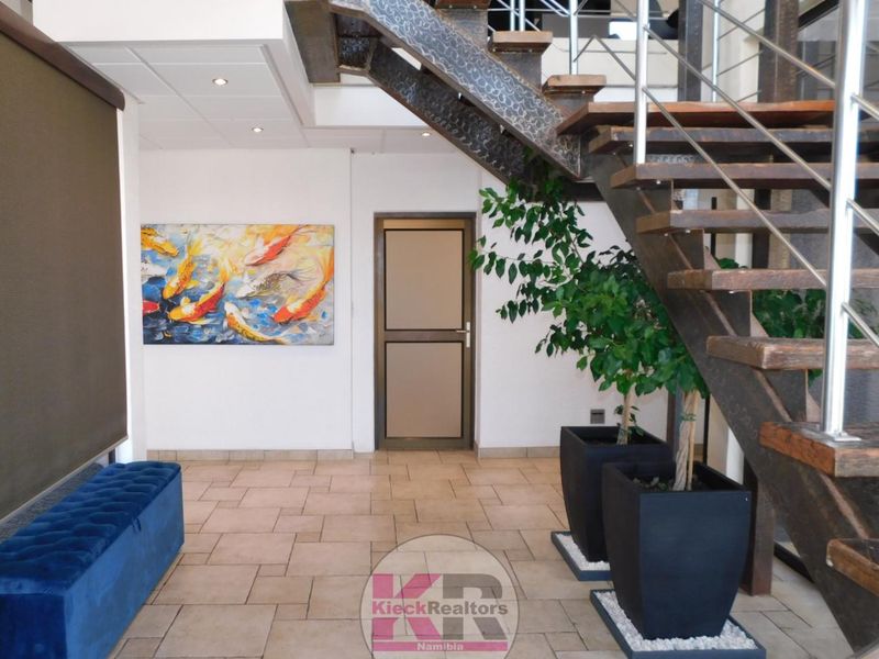 A modern entrance hall featuring a striking open-tread staircase with metal framing and stainless steel balustrades, complemented by neutral tiled flooring.