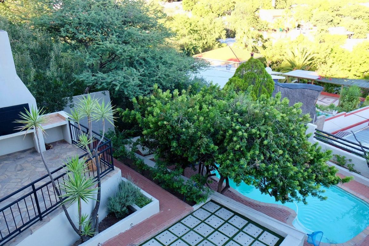 Elevated view of a backyard featuring a built-in braai area, paved patio, swimming pool, and established garden landscaping.