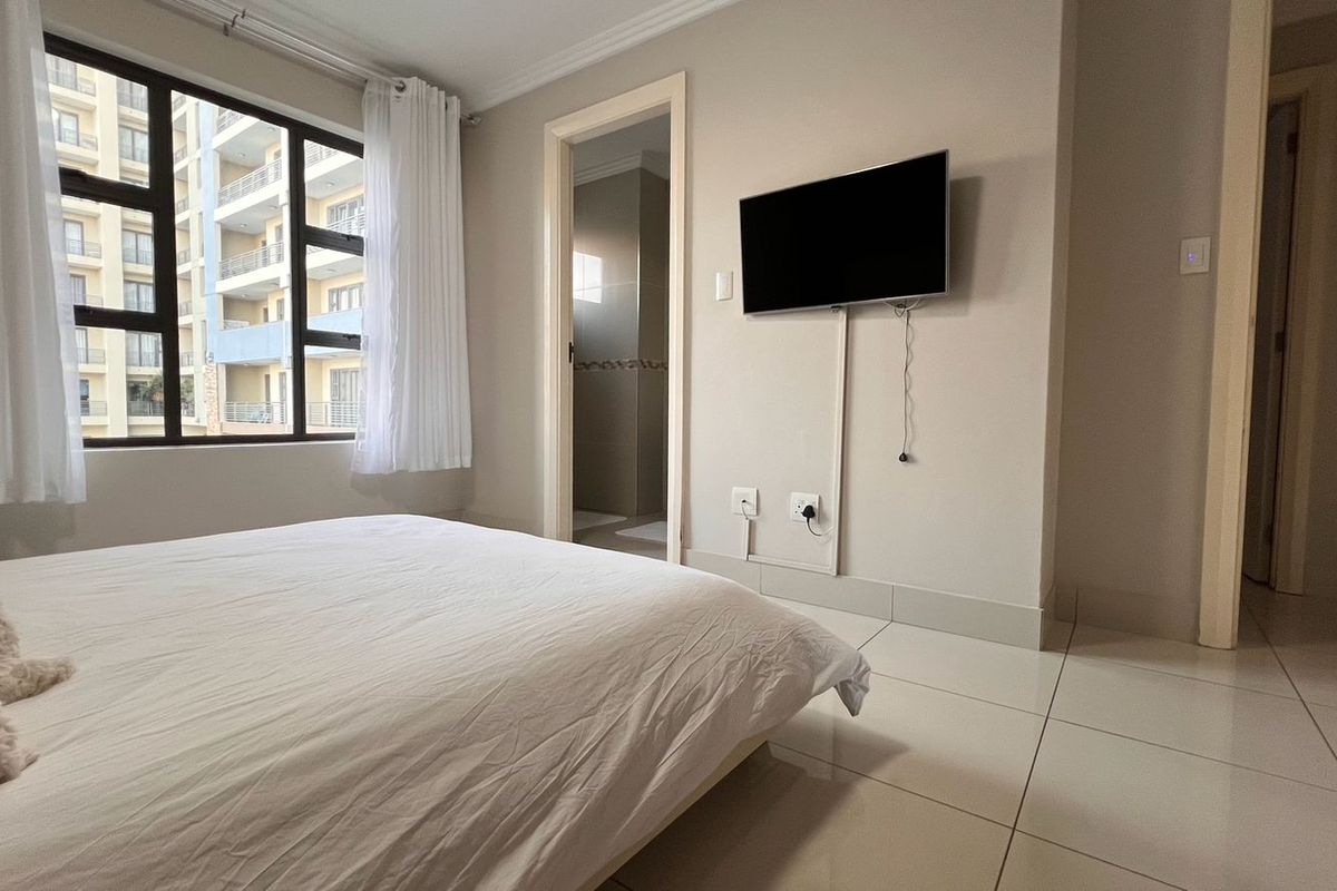 A bright bedroom featuring large windows, tiled flooring, and an en-suite bathroom entrance.