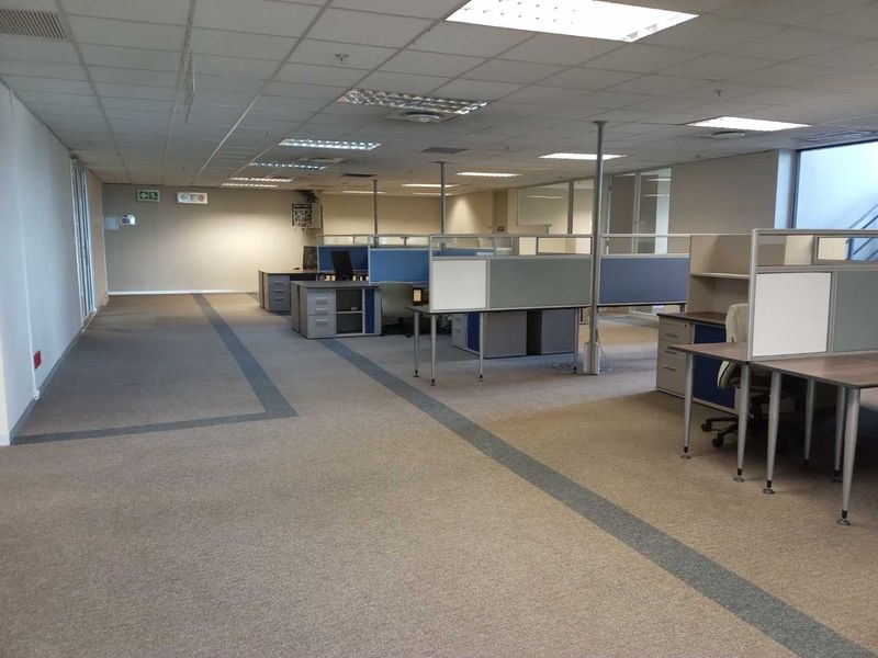 Open plan office space featuring modular cubicle workstations, suspended ceiling tiles, recessed lighting, and neutral carpeted flooring.
