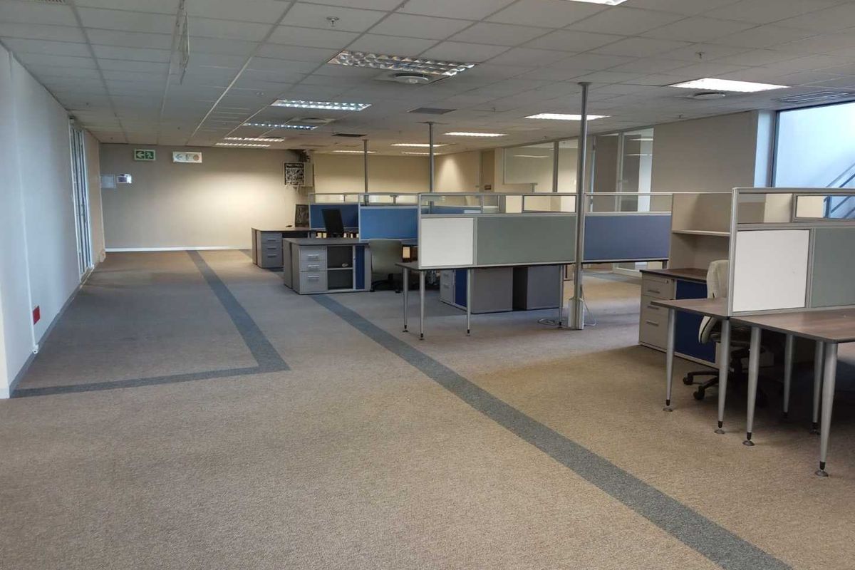 Open plan office space featuring modular cubicle workstations, suspended ceiling tiles, recessed lighting, and neutral carpeted flooring.