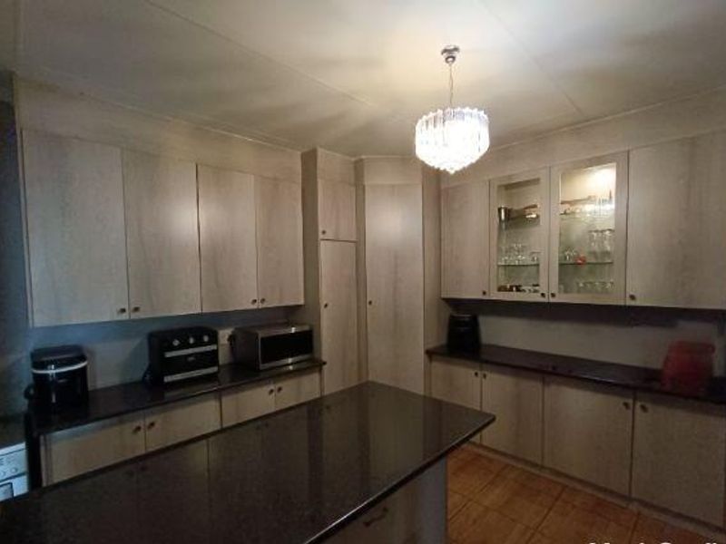 A functional kitchen featuring light wood-finish cabinetry, dark granite countertops, glass-front display units, and tiled flooring with a central island.