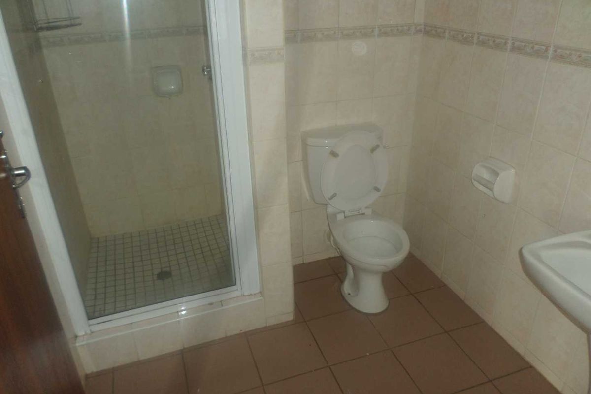 A functional bathroom featuring a shower enclosure, toilet, and pedestal basin with neutral wall and floor tiling.