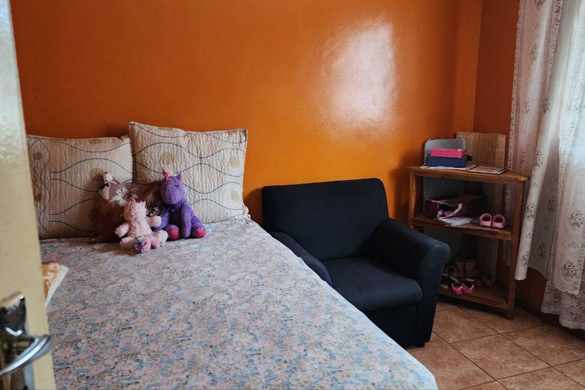 A bedroom featuring tiled flooring and orange painted walls, providing a functional space with natural light from the window.