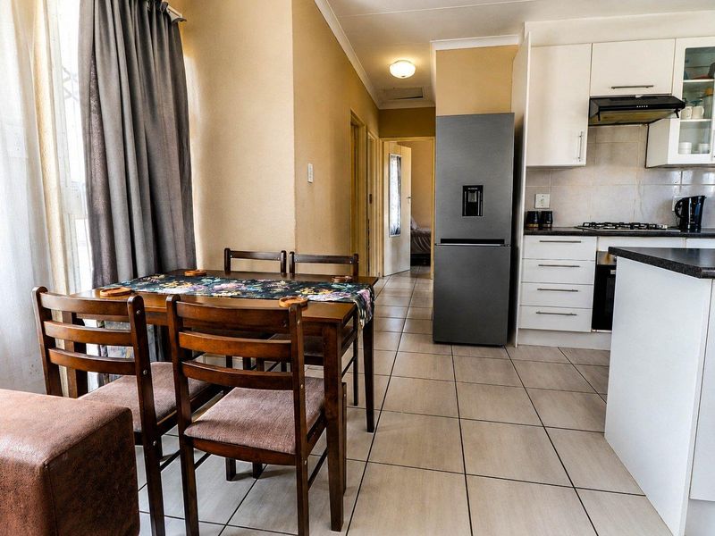 Open-plan kitchen and dining area featuring tiled flooring, modern white cabinetry, built-in oven and hob, and direct access to the hallway.