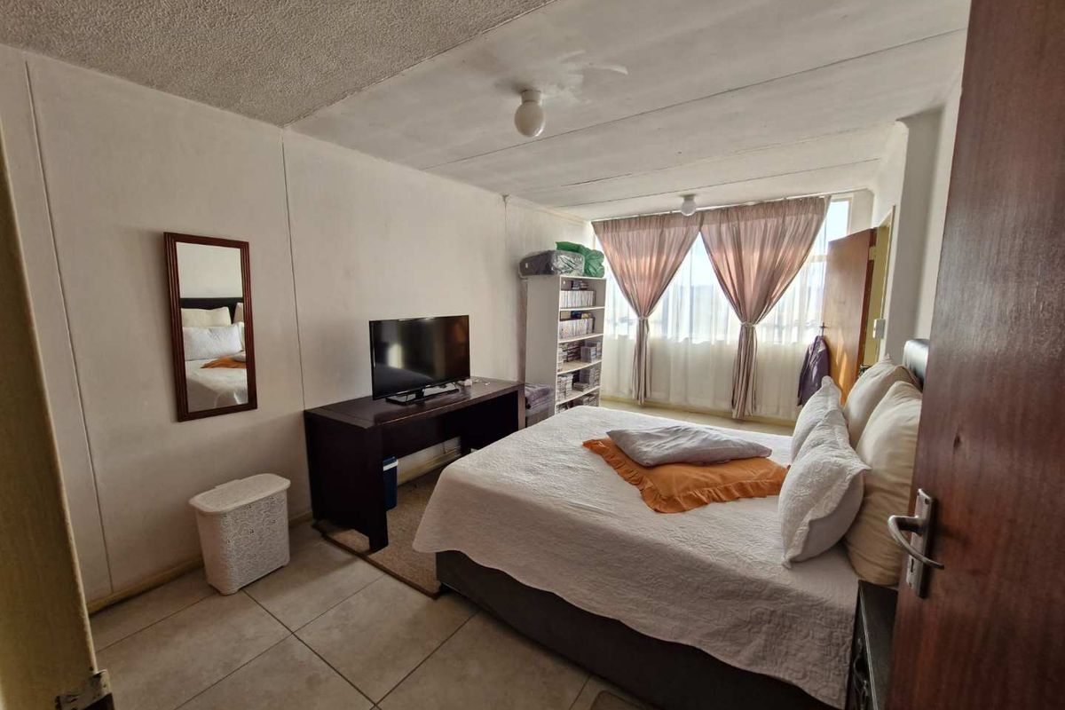 A bedroom featuring tiled flooring and a large window, providing natural light. The room requires cosmetic updates to improve its overall condition.