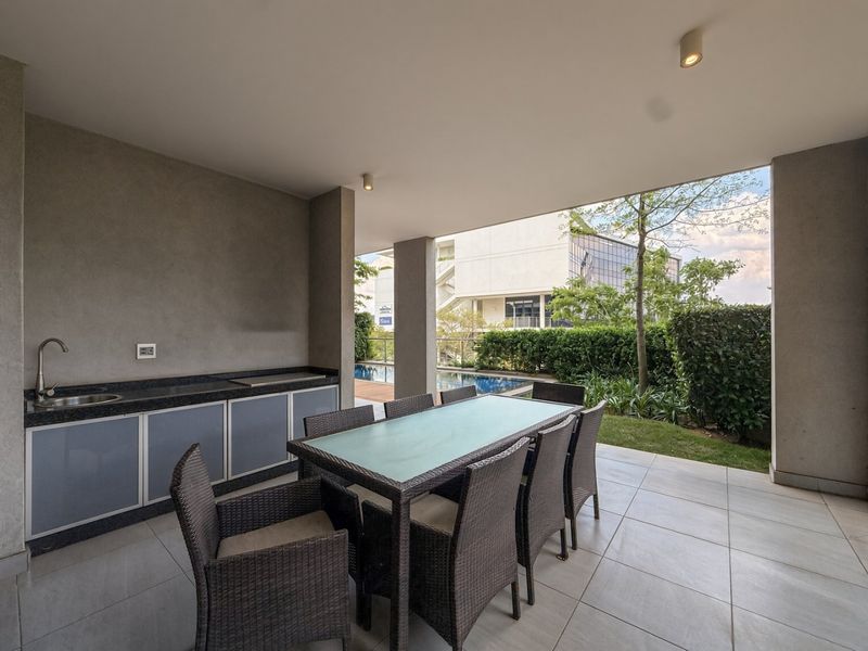 Covered patio featuring a built-in kitchenette with granite countertops, sink, and tiled flooring, overlooking a private garden and swimming pool area.