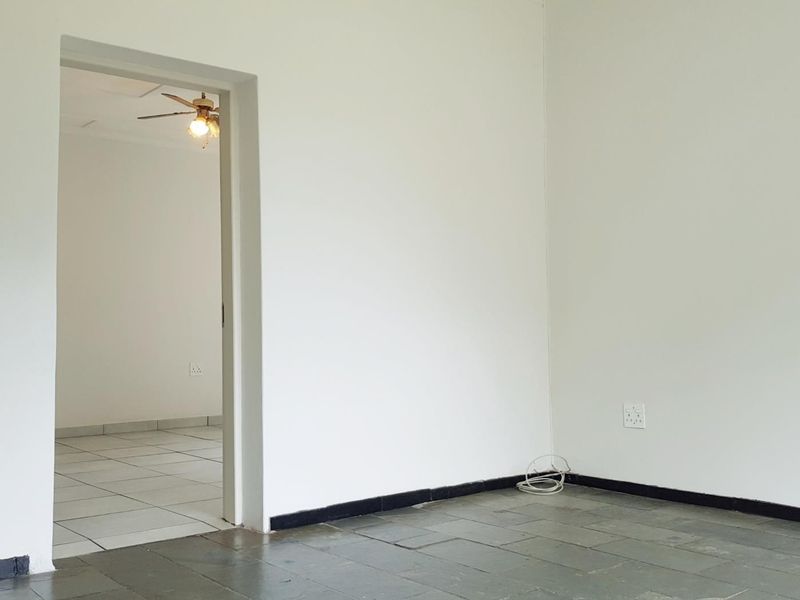 An empty living area featuring stone tile flooring and a connecting room with ceramic tiles, providing a blank canvas for interior design.