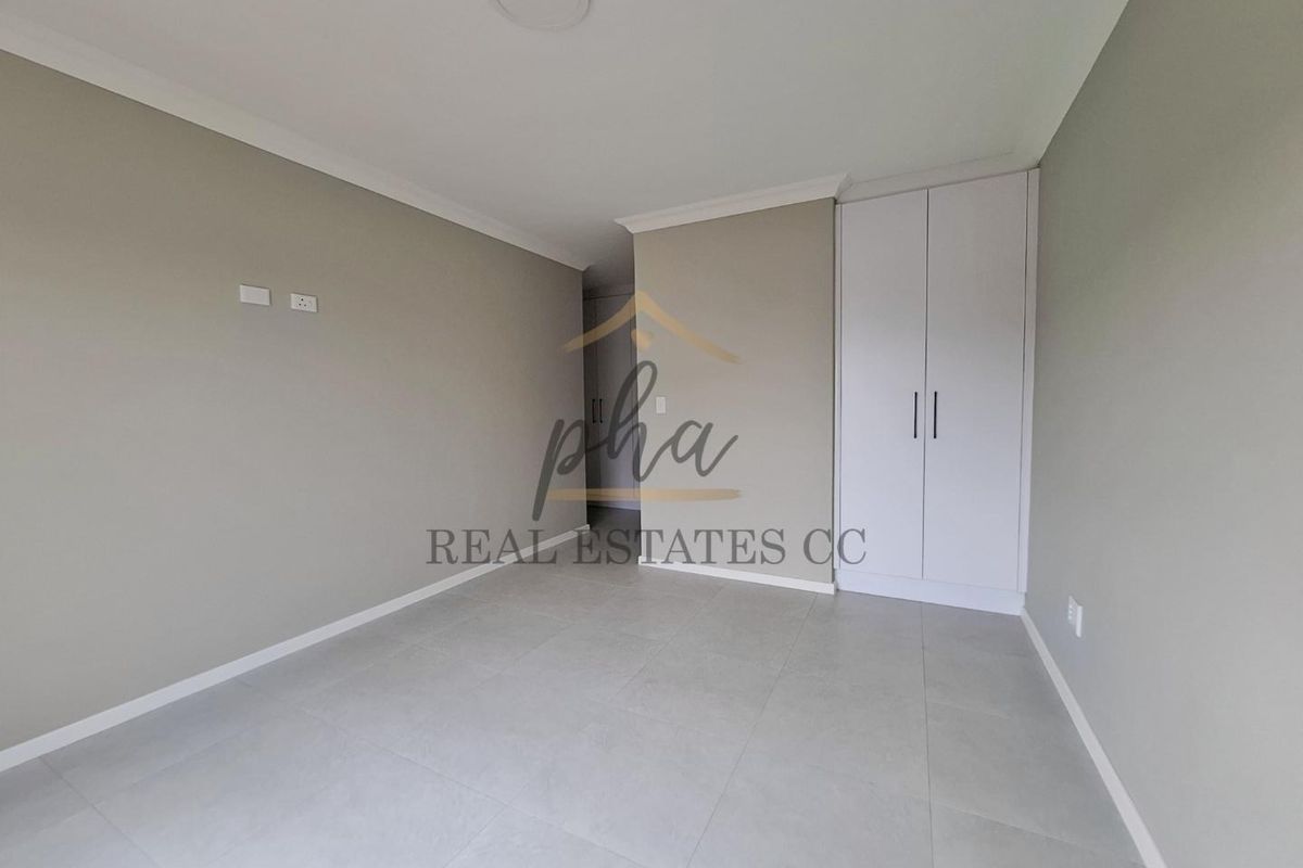 A clean, empty bedroom featuring neutral wall paint, modern tiled flooring, and a built-in white wardrobe.